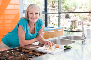 一位熟齡女性在明亮的廚房中翻閱食譜，展現持續學習與享受生活的自在狀態