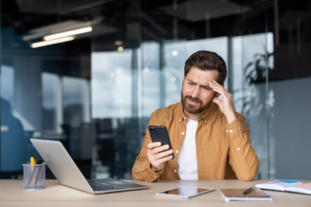 一名男性在辦公室盯著手機時露出吃力與不適表情，顯示長時間使用手機造成視力疲勞。